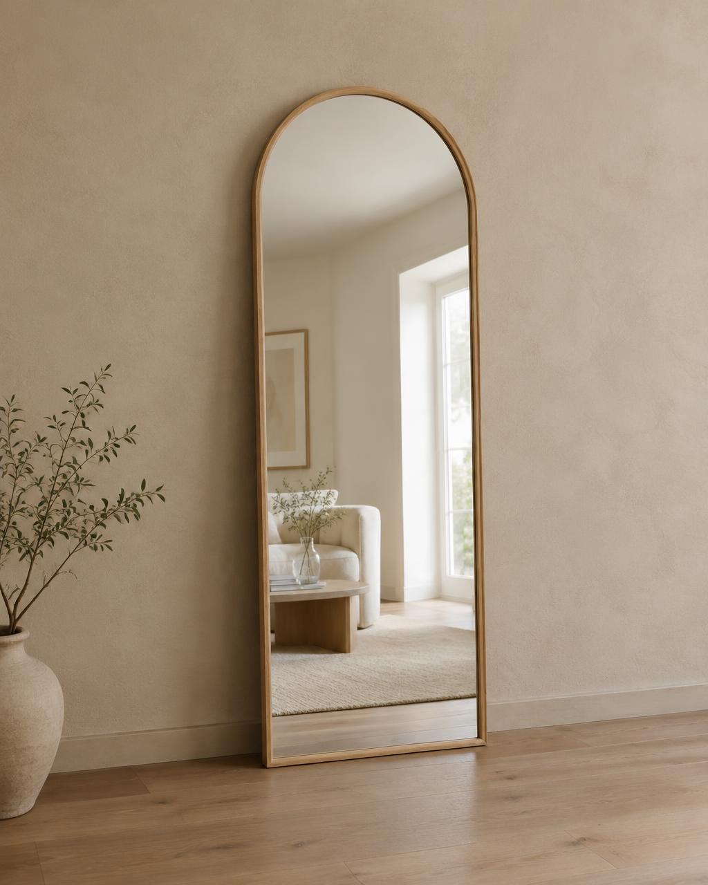 Tall arched oak-framed mirror leaning against a beige plaster wall