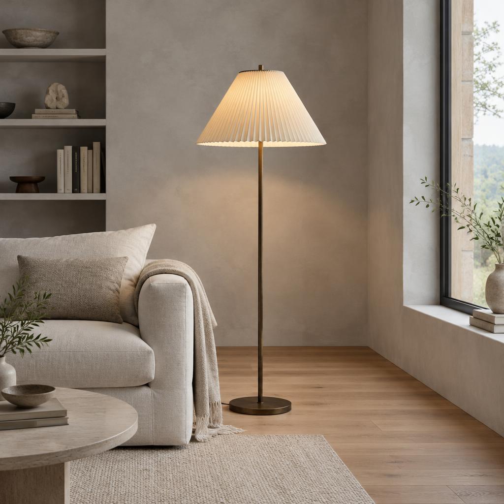 Pleated floor lamp with a slim bronze stem beside a linen sofa in a sunlit reading room