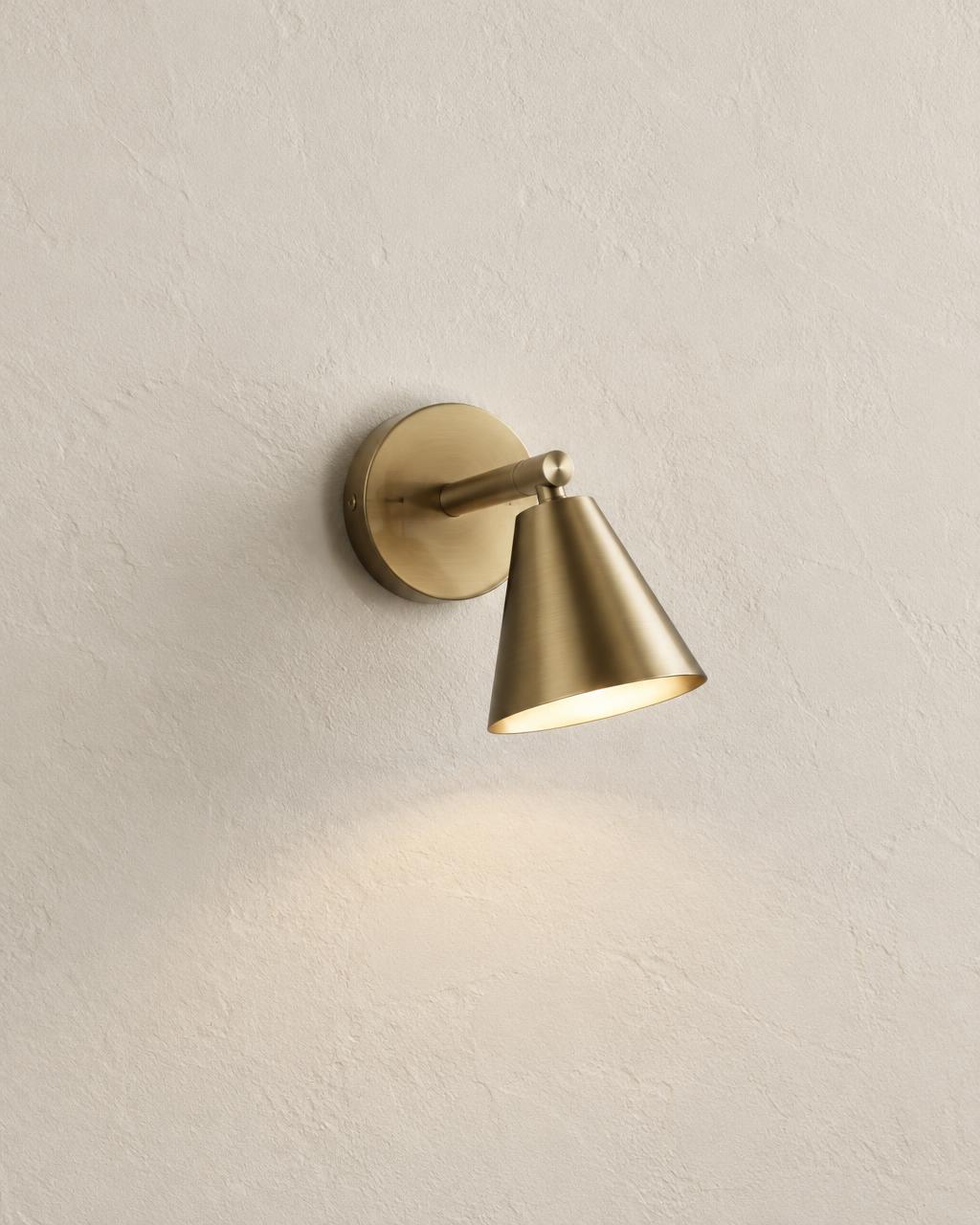 Brushed brass wall sconce with cone shade on textured plaster