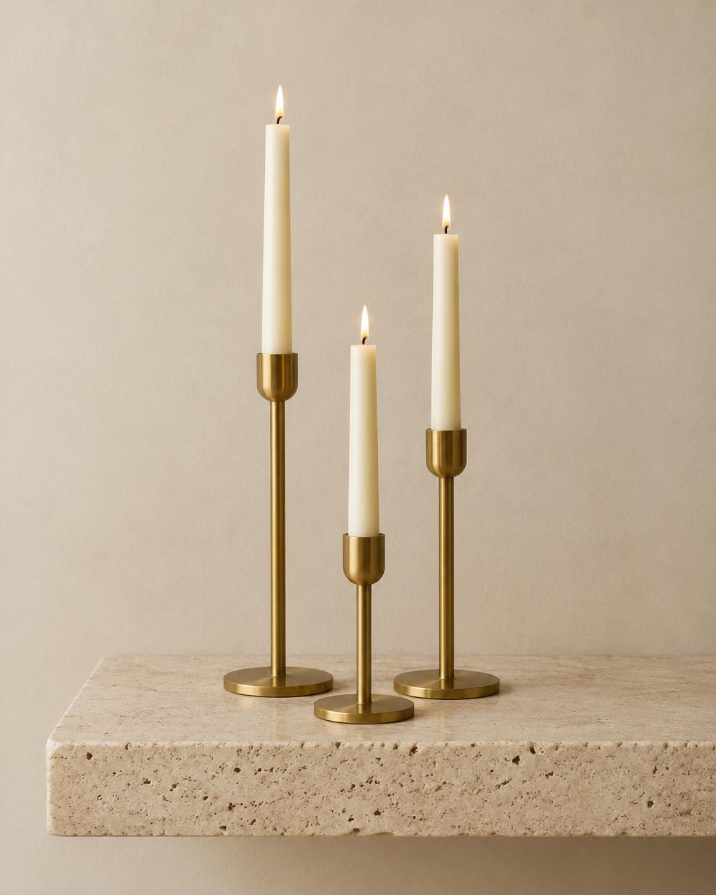 Three brass candle holders with ivory tapers on a travertine shelf