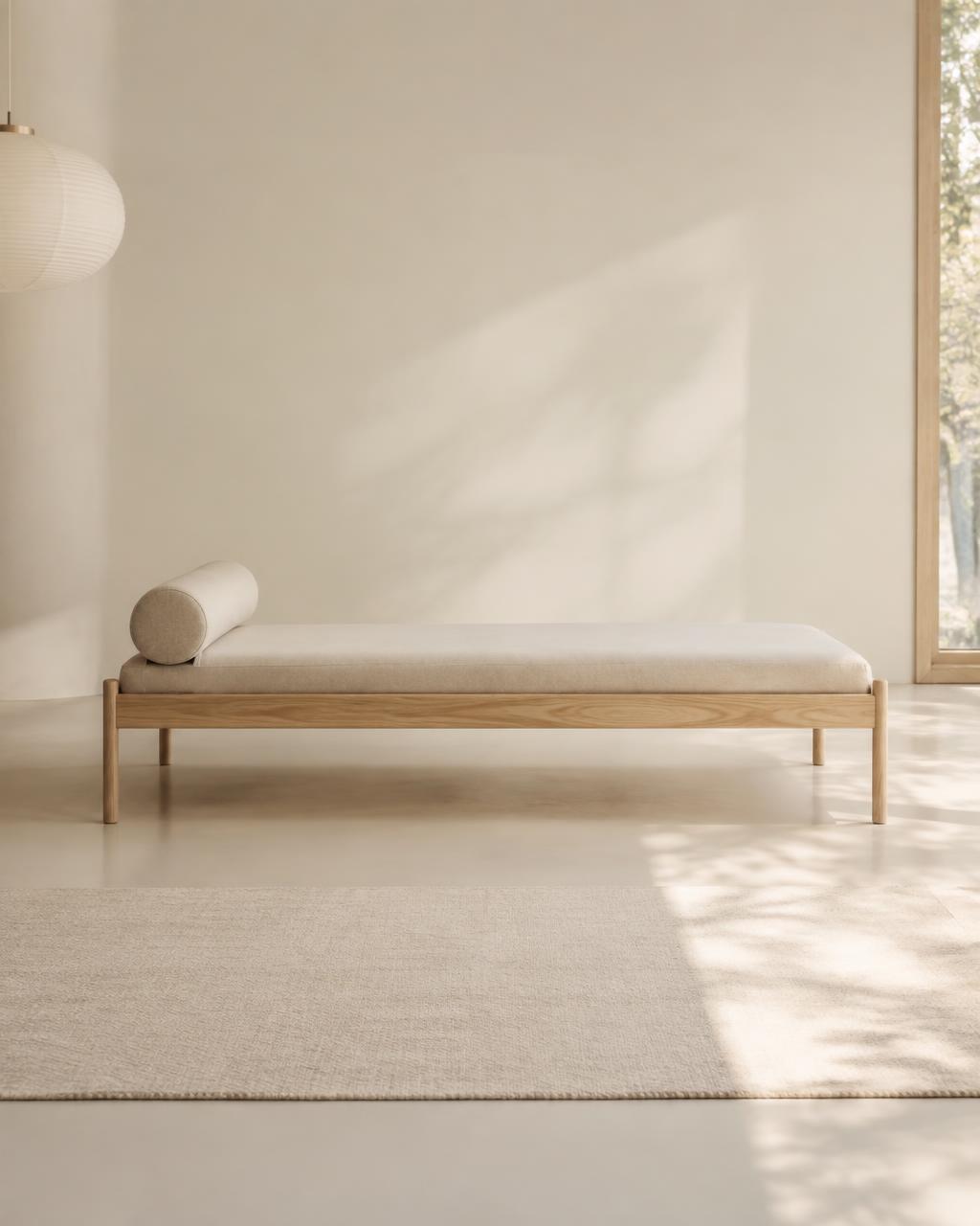 Ash daybed with linen mattress and bolster in a sunlit room